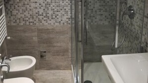 Un bagno moderno con doccia vetrata, un lavandino bianco e due servizi igienici.