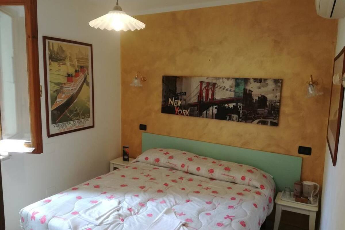 Un dormitori amb llit, capçalera, calaixera, làmpada i dues làmines de llum penjades a la paret.