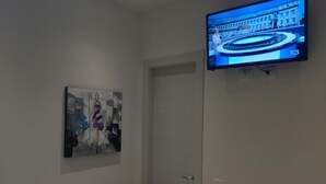 Una stanza con una televisione fissata al muro che mostra un canale di notizie, una porta e un quadro appeso al muro.