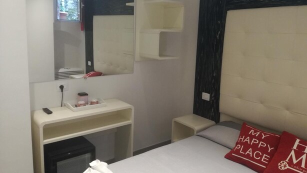 Una camera d'albergo con un letto, un comodino, uno specchio e una piccola scrivania con un telefono e una tazza.