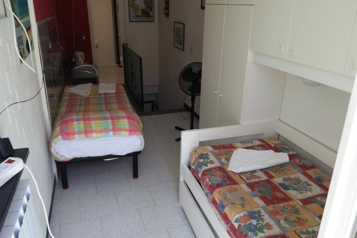 Habitació petita i senzilla amb dos llits individuals, un armari blanc, un ventilador i un radiador.