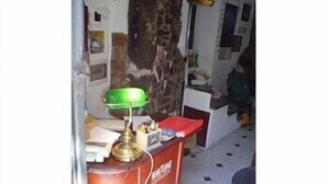 Una scrivania in legno con una lampada da tavolo verde, una cartella rossa e una piccola scatola bianca.