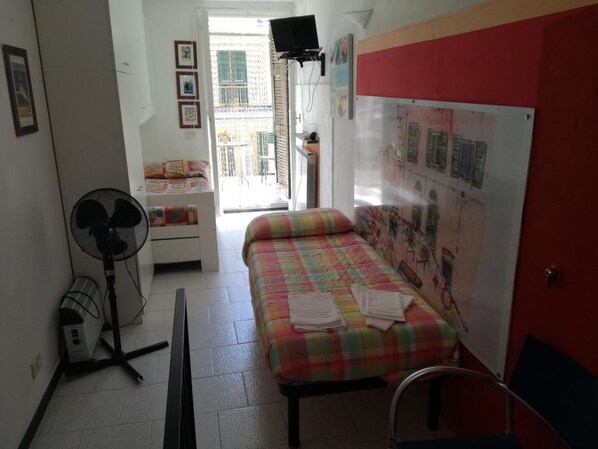 A small, neatly arranged room with a bed, a fan, a radiator, and a door leading to an outdoor area. - Ca' dei Lisci-B&B (Riomaggiore)