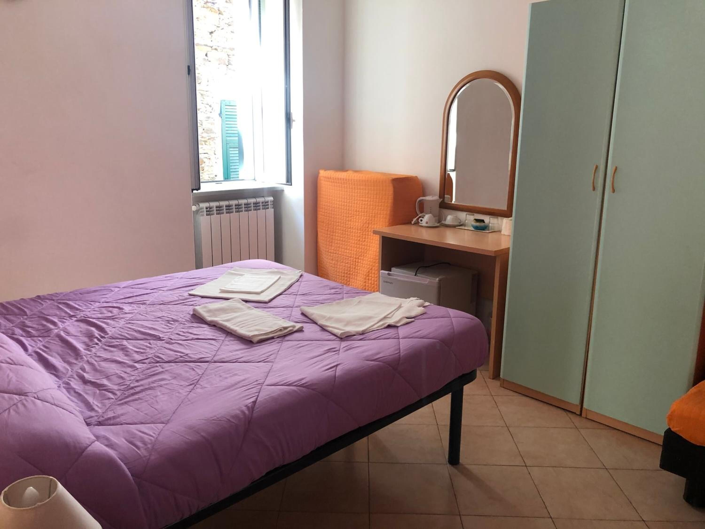 Una camera da letto con un letto, una finestra, un termosifone, una scrivania con uno specchio e un armadio.
