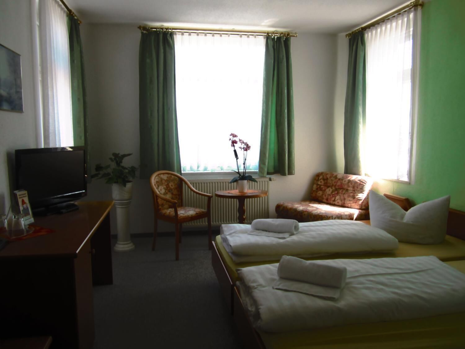 Une chambre d’hôtel avec deux lits, une télévision, une chaise, une table avec une plante et une fenêtre avec des rideaux.