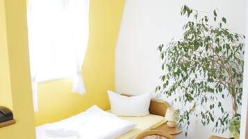 Una habitación pequeña con cama, escritorio, silla y planta.