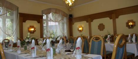 A dining area with tables set for a meal, featuring white tablecloths, neatly arranged cutlery, and floral centerpieces.