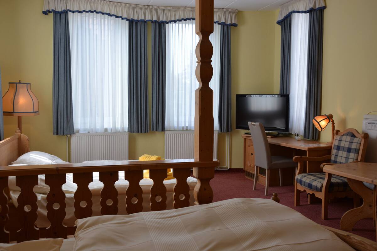 Quarto de hotel com uma cama, uma mesa de trabalho com cadeira, uma televisão e um abajur.