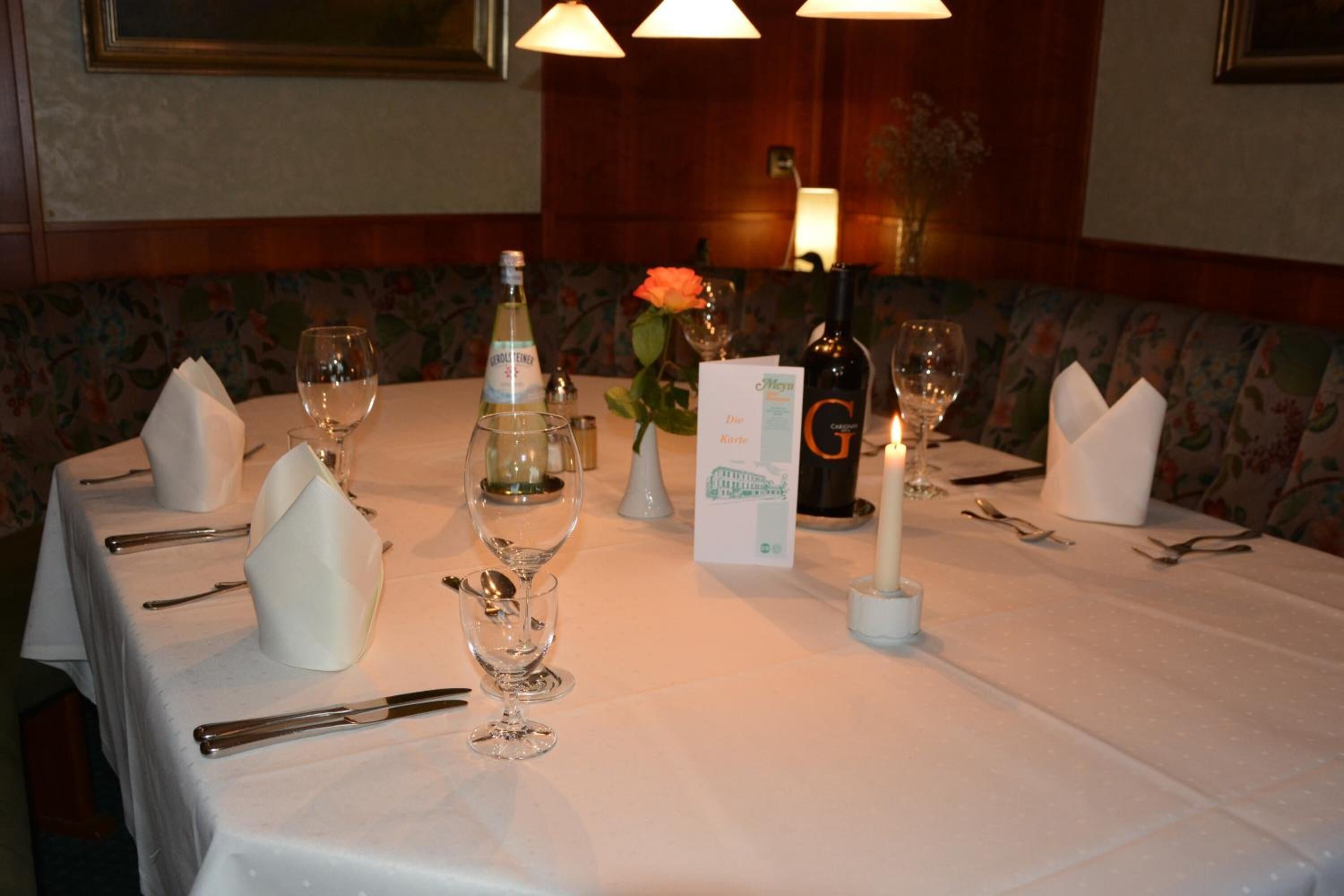 A dining table set with white tablecloth, wine glasses, a candle, and a menu.