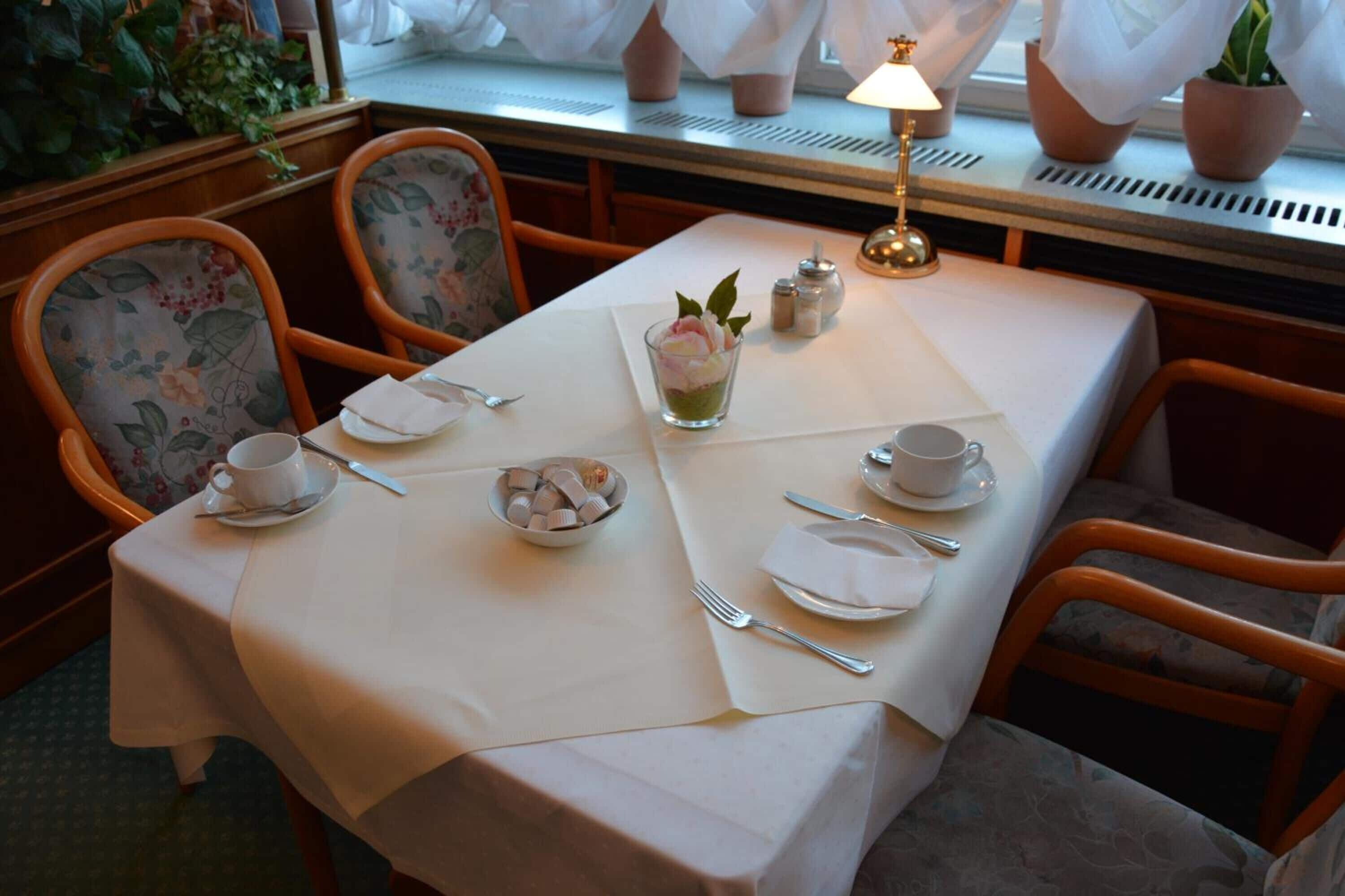 Mesa de comedor dispuesta con mantel blanco, sillas con estampado floral y un pequeño florero con una flor.