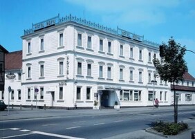 Un edificio blanco de varios pisos con un estilo arquitectónico clásico, que cuenta con un balcón en el piso superior y una entrada a nivel de calle.