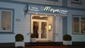 A hotel and restaurant named "Meyn" with a white facade, double doors, and a small porch with potted plants.