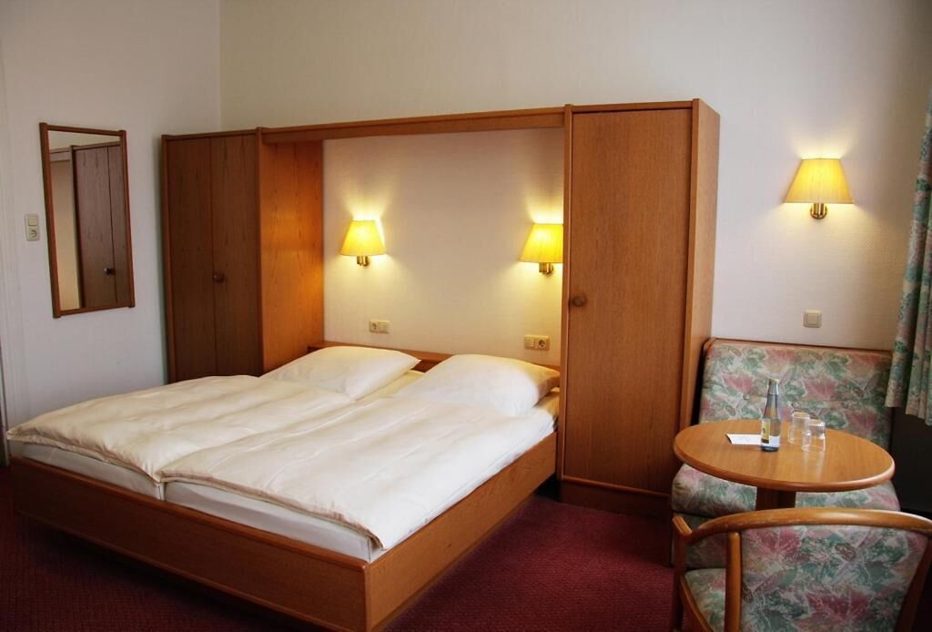Habitación de hotel con cama, dos lámparas de pared, una silla y una mesita.