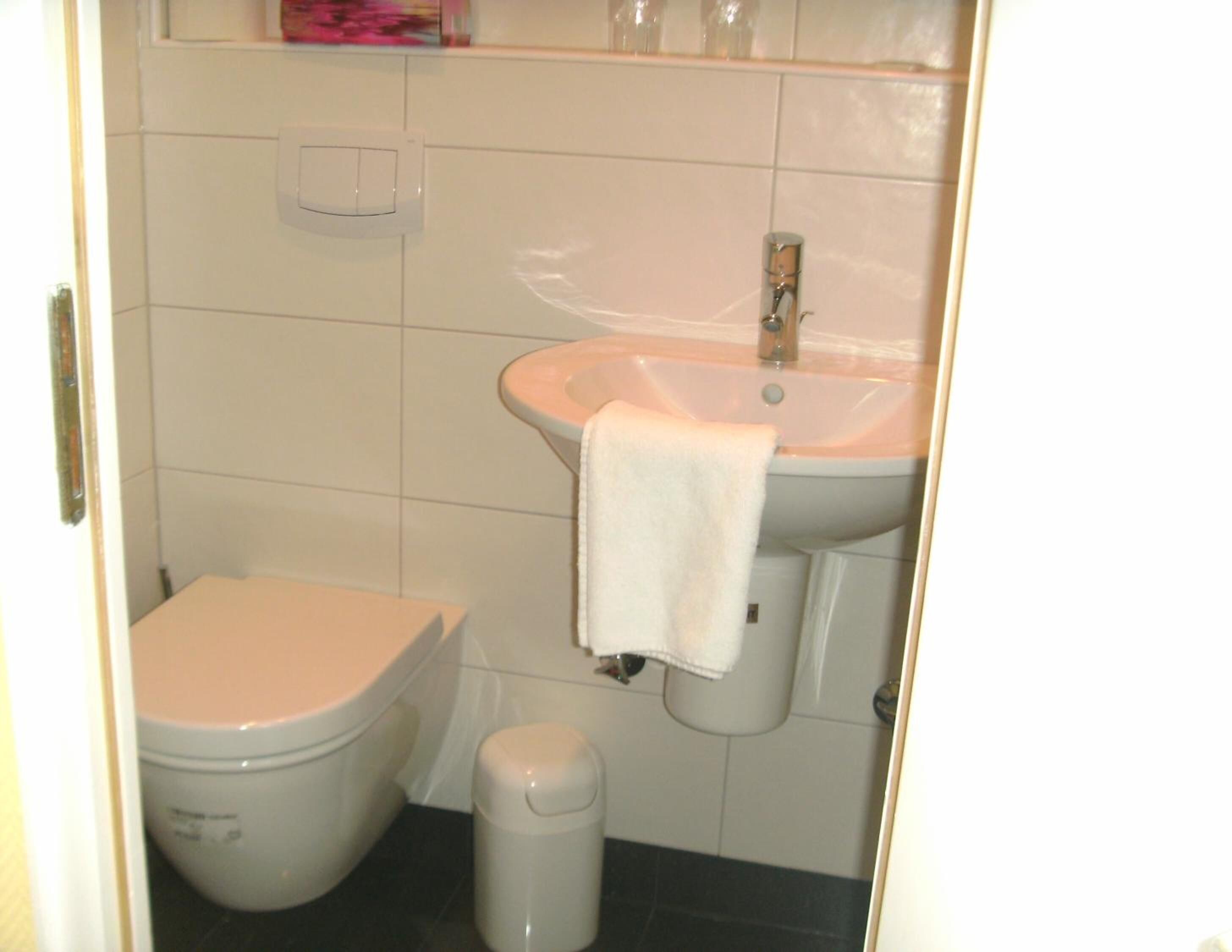 A bathroom with a white toilet, a sink with a towel, and a trash bin.