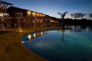 A poolside area with lounge chairs and umbrellas, a pool, and a building with multiple balconies and lights. - Oka da Mata - Hotel Pousada (Tibau do Sul)
