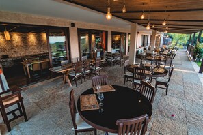 An outdoor dining area with multiple tables and chairs, stone walls, and hanging light fixtures. - Oka da Mata - Hotel Pousada (Tibau do Sul)