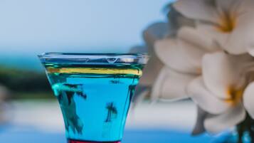 A clear glass with a blue liquid, a white flower, and a blurred background.