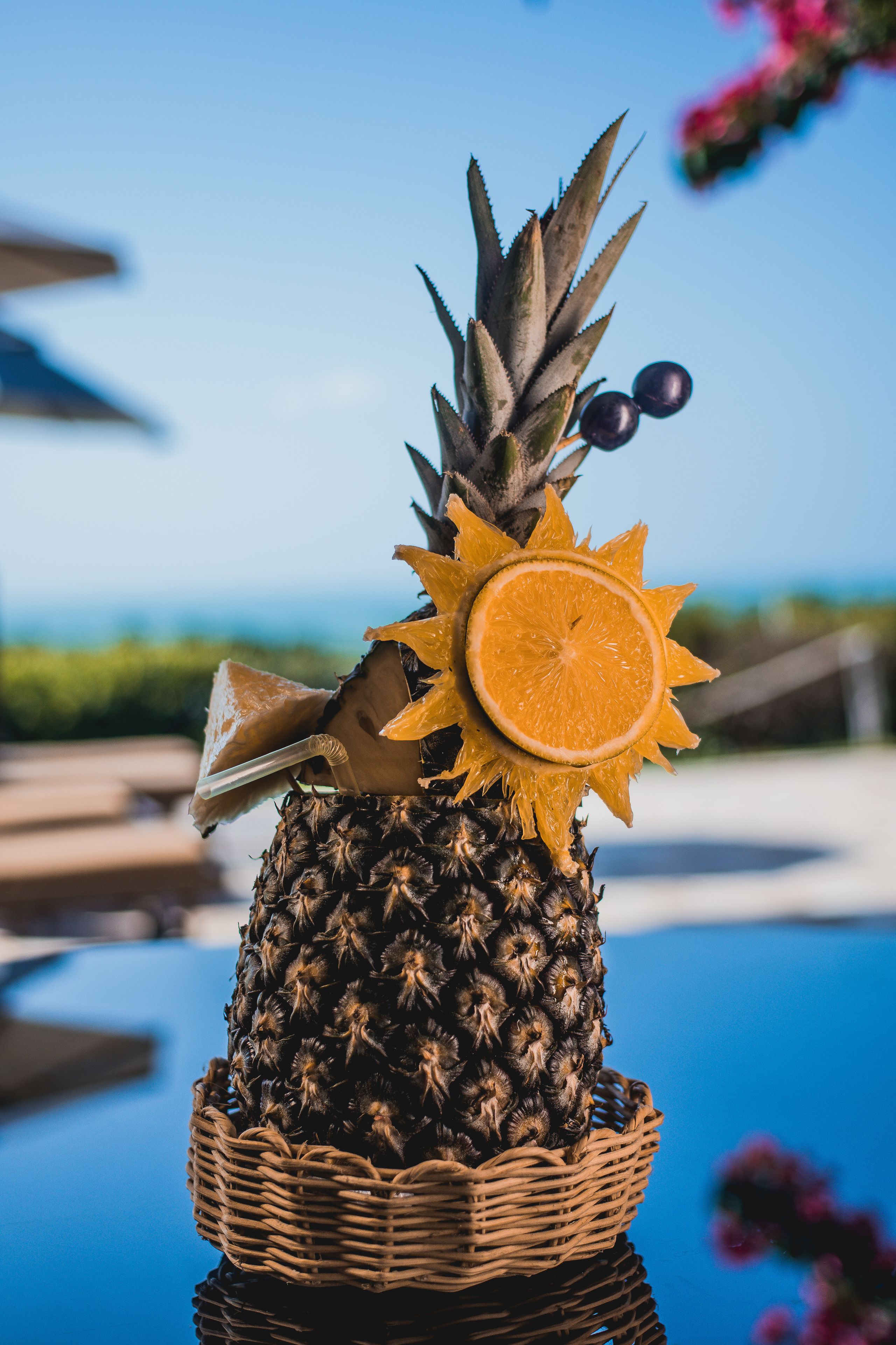 Un ananas surmonté d’une tranche d’orange, placé dans un panier en osier sur une surface réfléchissante.