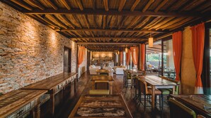 A rustic interior with stone walls, wooden beams, and a long dining area with tables and chairs.