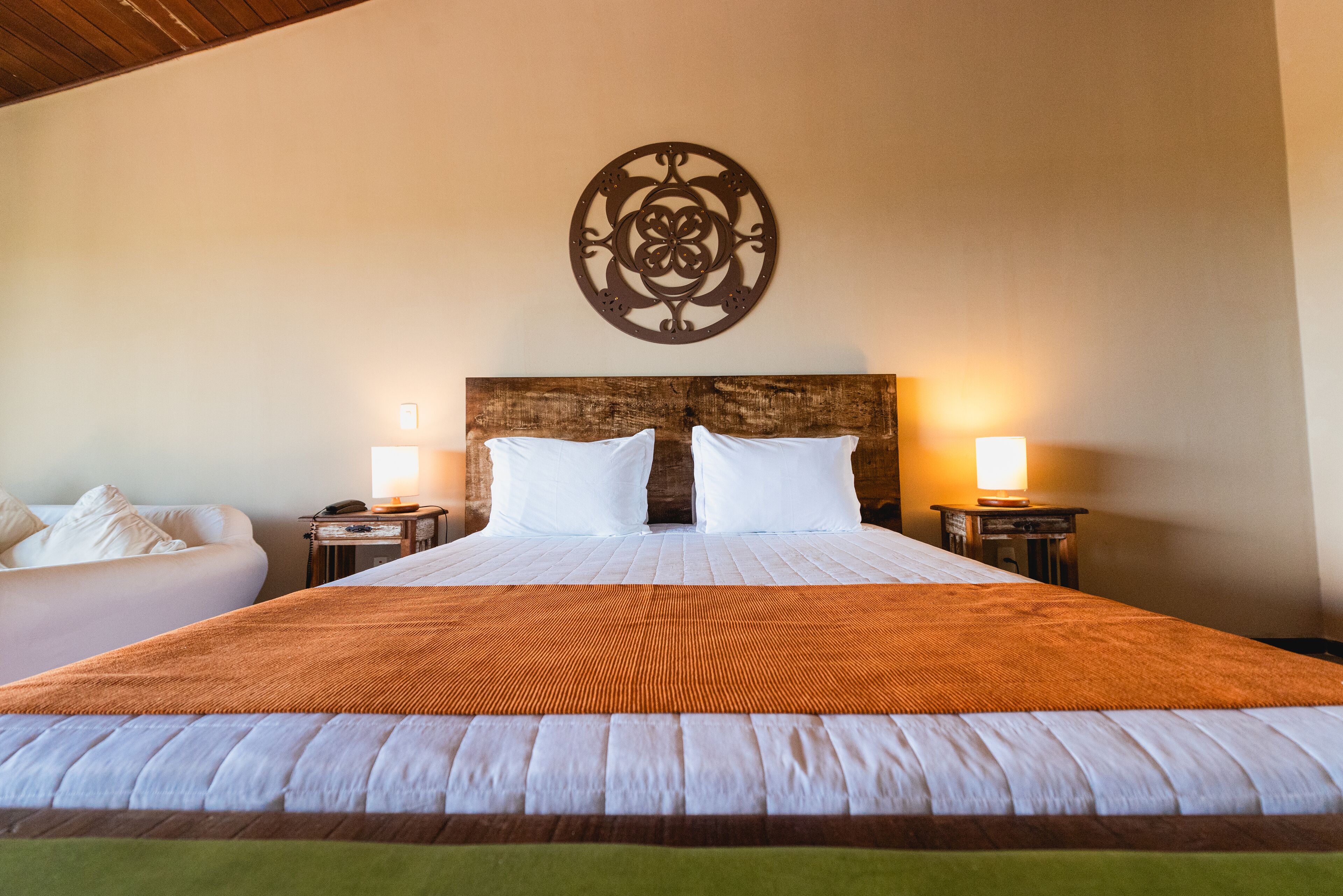 A large bed with a wooden headboard, two bedside lamps, and a decorative wall piece above the bed.