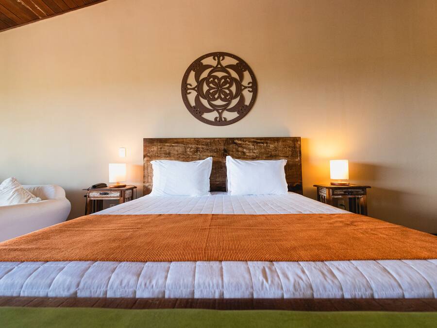 A large bed with a wooden headboard, two bedside lamps, and a decorative wall piece above the bed.