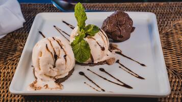 A dessert plate with two scoops of ice cream and a chocolate dessert, garnished with mint leaves and chocolate drizzle, on a white plate.