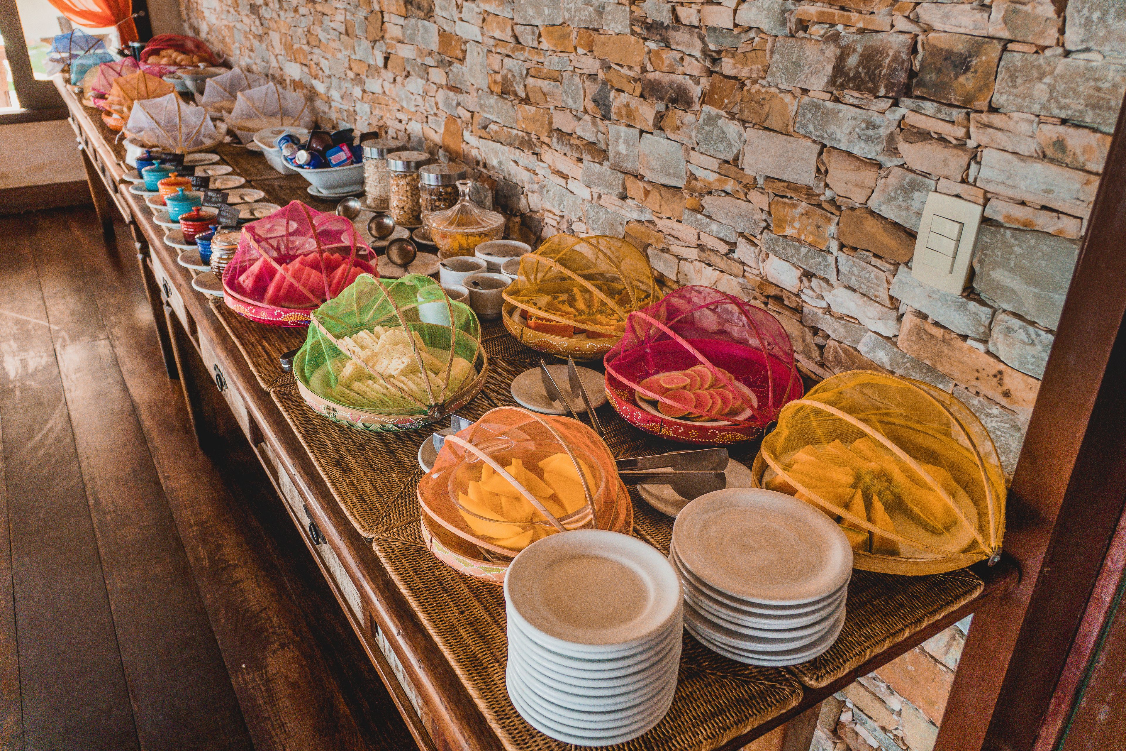 Una mesa de madera exhibe diversos alimentos y platos, con un muro de piedra como fondo.