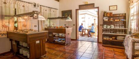 Una cocina con una estufa grande, un fregadero y una encimera con varios utensilios de cocina. Una puerta conduce a un comedor con una mesa y sillas.