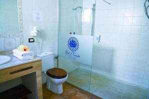 A bathroom with a toilet, a sink, a shower, and a glass door with a logo. - Hotel Rural El Navío- Adults Only (Guia de Isora)