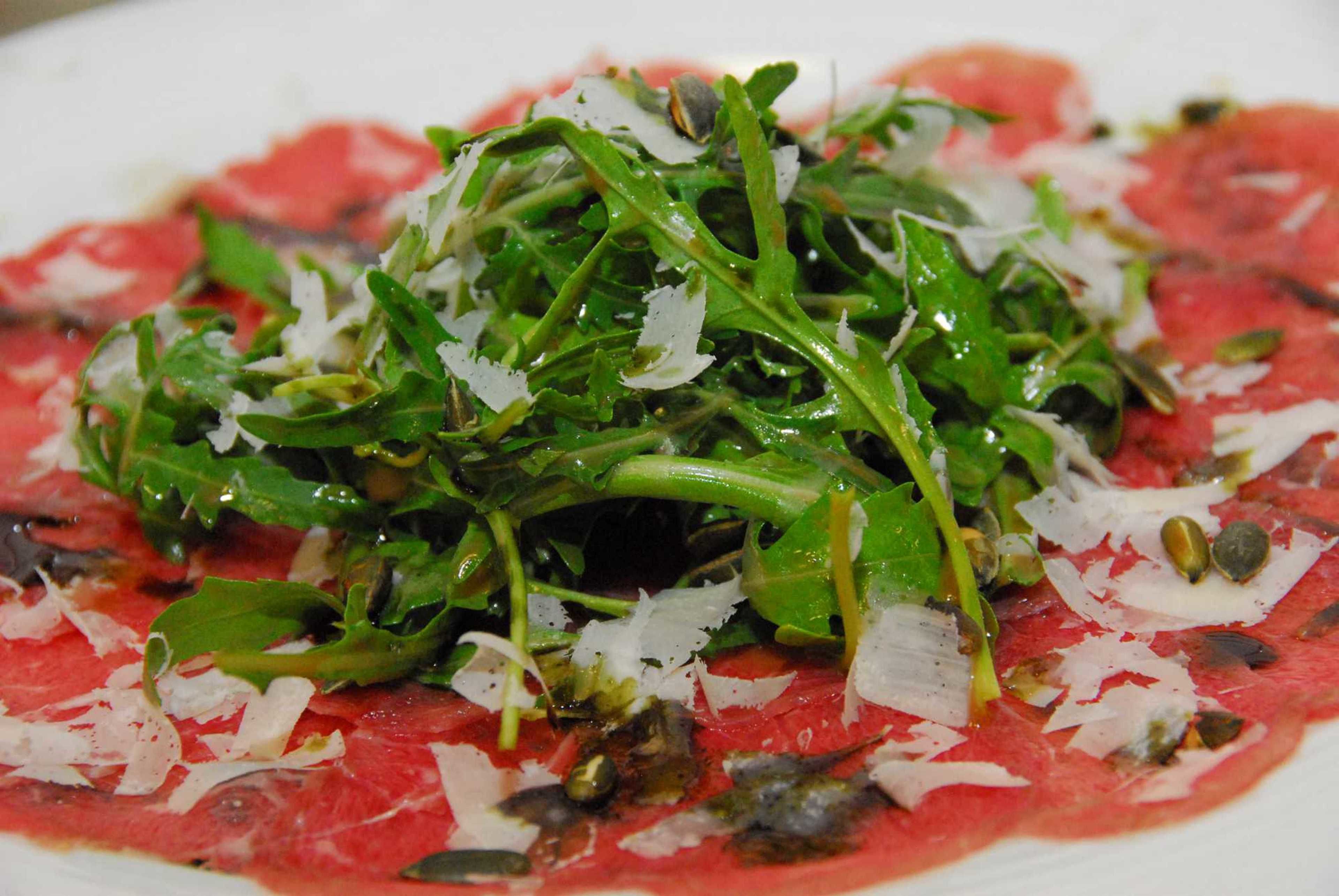A plate of raw meat topped with greens and cheese.