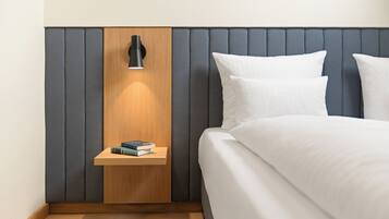 A neatly made bed with white linens, a bedside table with a book, and a wall-mounted lamp.