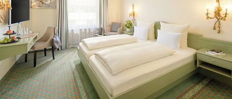 A hotel room with two beds, a desk with a TV, a chair, and a window with curtains.