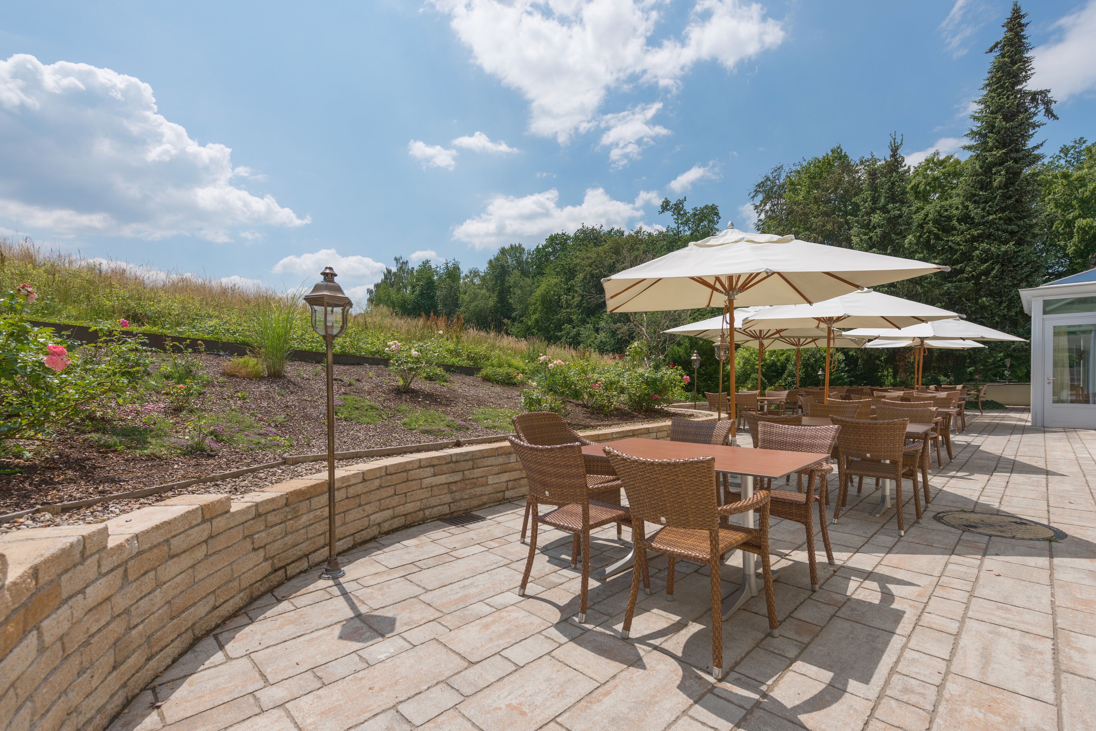 An outdoor patio with wicker furniture and umbrellas, surrounded by a brick wall and greenery.