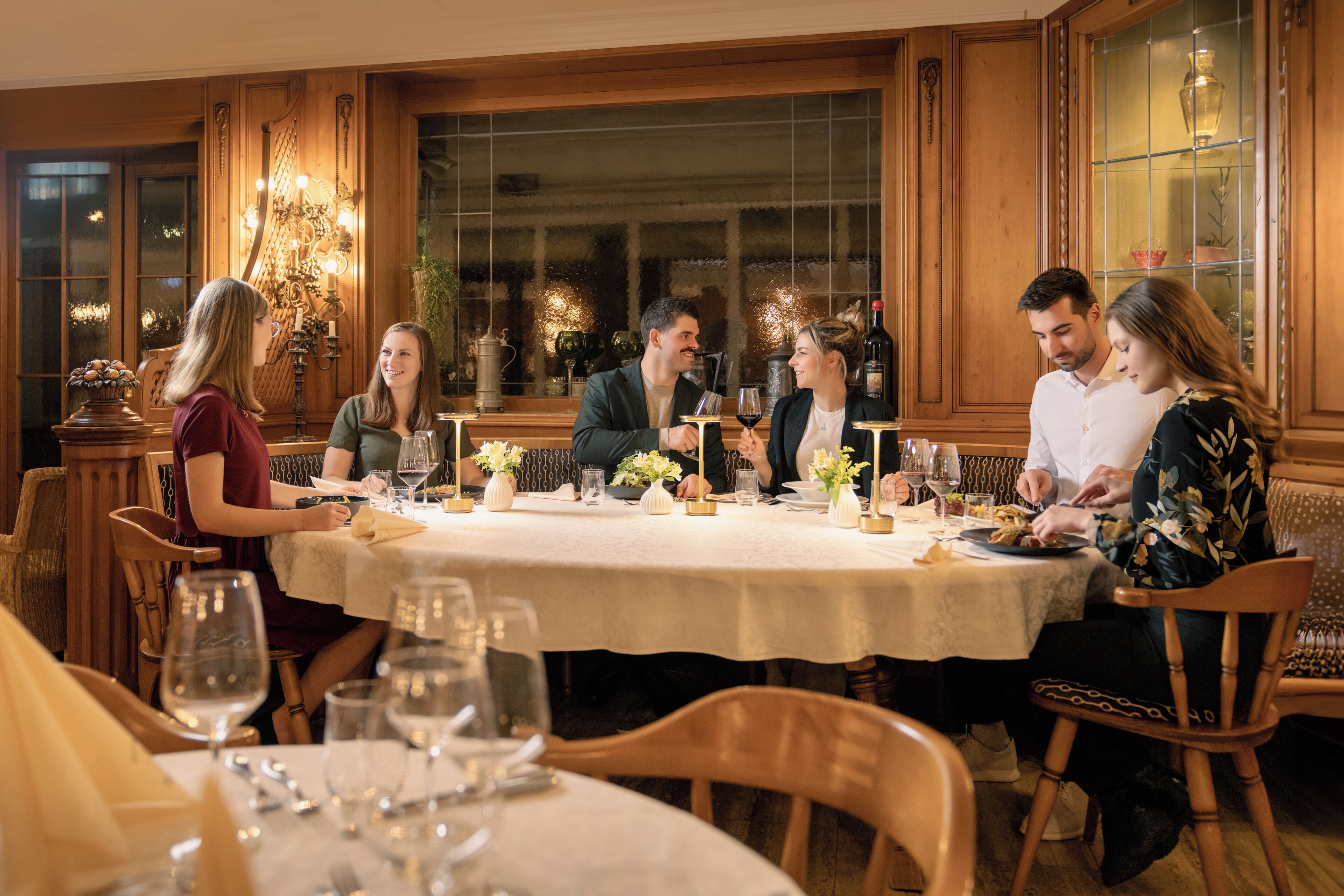A dining area with a round table, wooden chairs, and a chandelier.