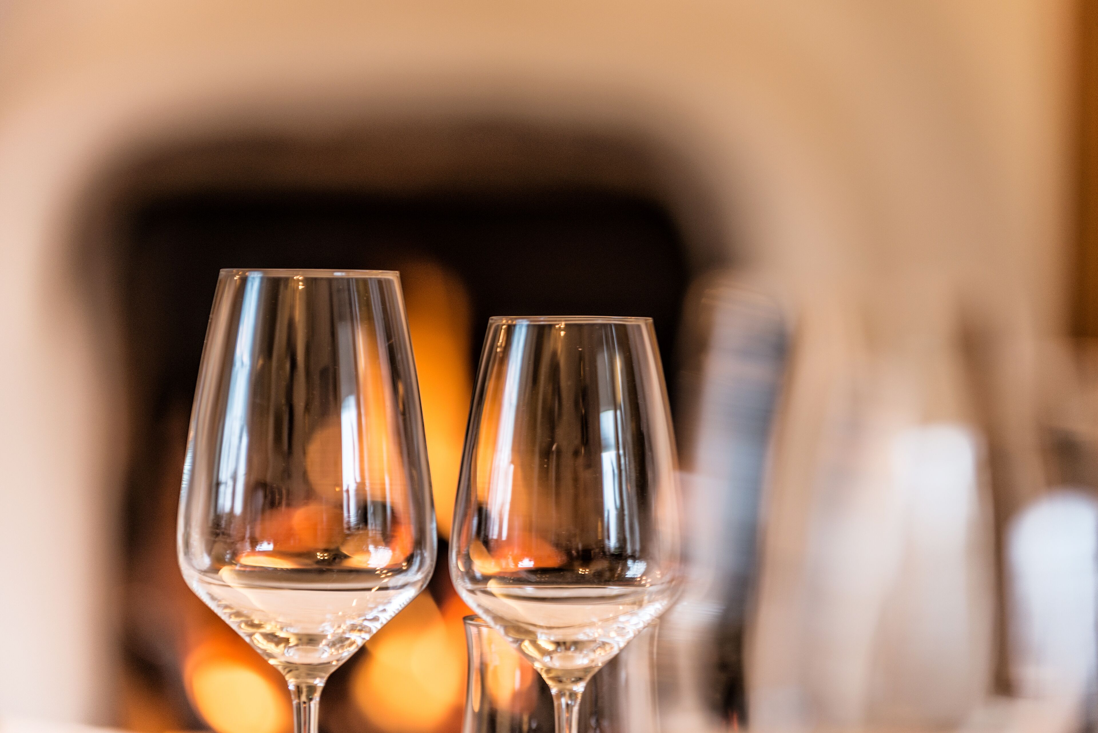Two empty wine glasses on a table with a blurred background of a fireplace.