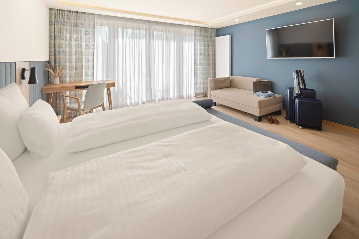 A hotel room with two beds, a desk, a sofa, a TV, and luggage.