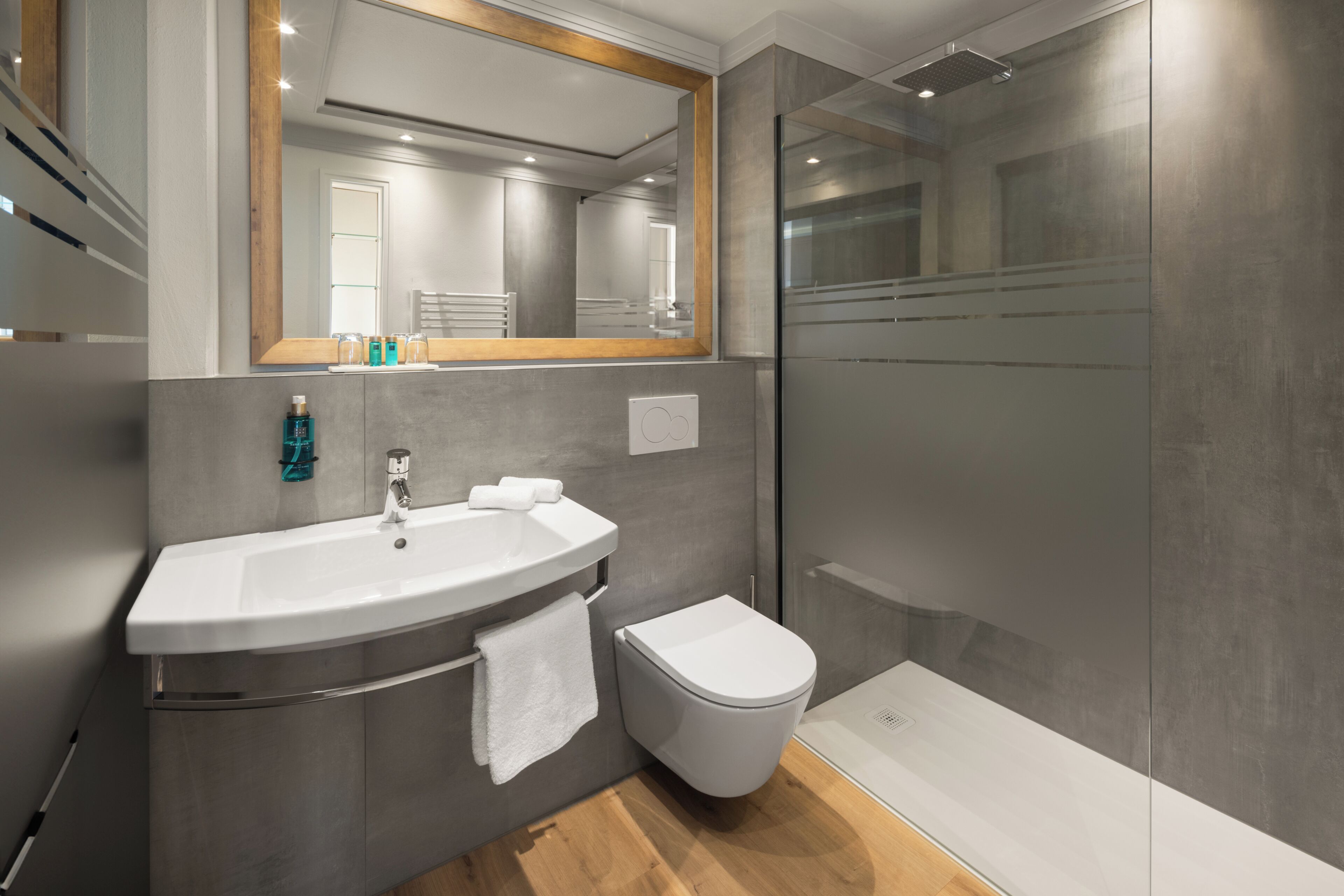 A modern bathroom with a large mirror, a sink, a toilet, and a glass-enclosed shower.