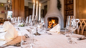 Una mesa de comedor dispuesta con copas de vino, platos y cubiertos, con una chimenea al fondo.