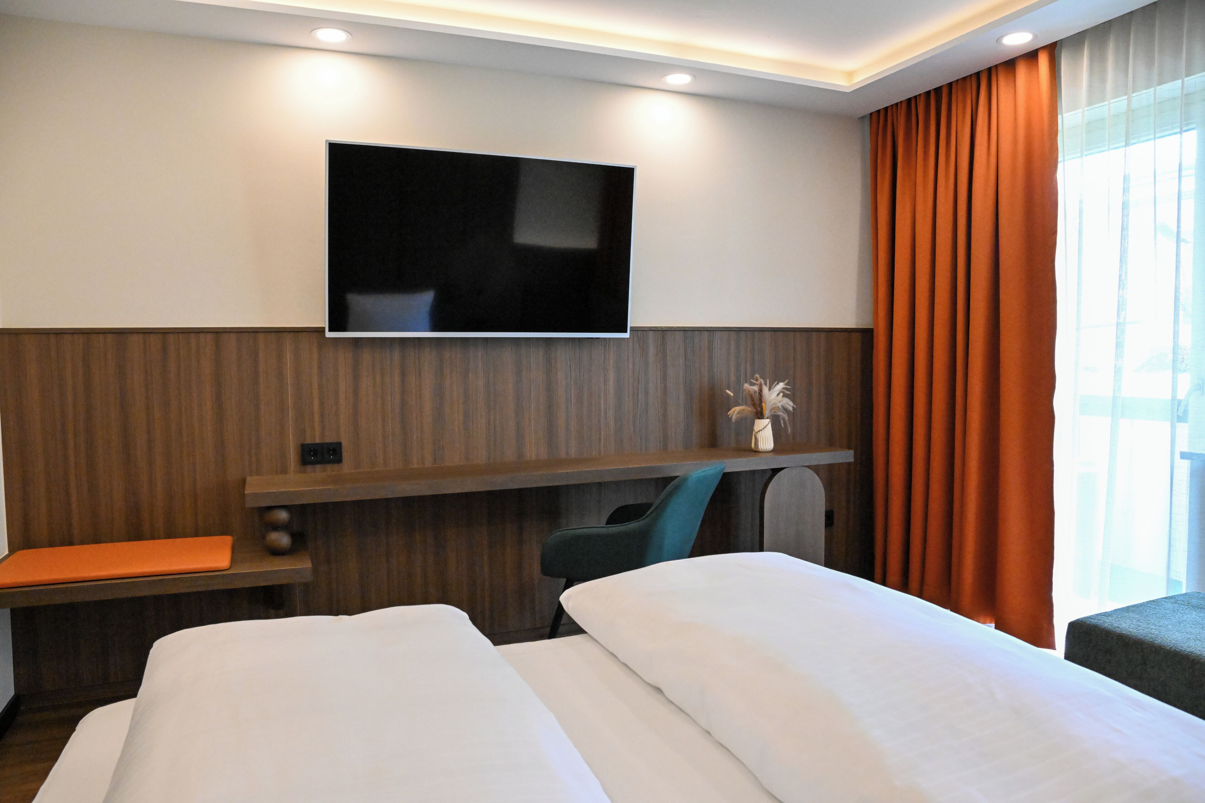 Habitación de hotel con televisor de pantalla plana montado en la pared, un escritorio con silla y una cama con ropa blanca.