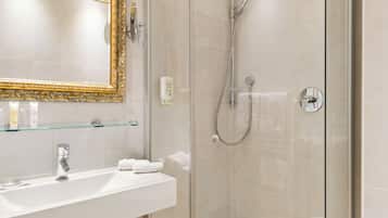 Un baño moderno con ducha envuelta en vidrio, un lavamanos blanco y un espejo con marco dorado, además de suelo con baldosas color beige.
