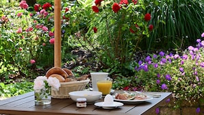 Una mesa de desayuno al aire libre con pan variado, un vaso de jugo de naranja y un plato de comida.