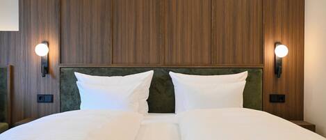 A hotel room with a wooden headboard, two bedside lamps, and a neatly made bed with white linens.
