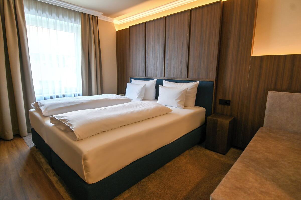 A hotel room with a large bed, wooden headboard, and a bedside table.