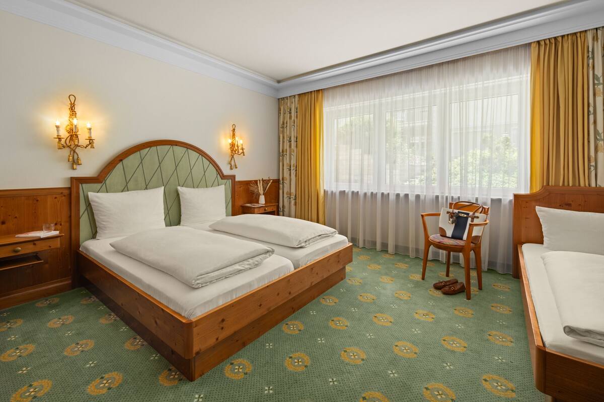 A double bed with a wooden headboard, two bedside tables, a chair, and a window with curtains.