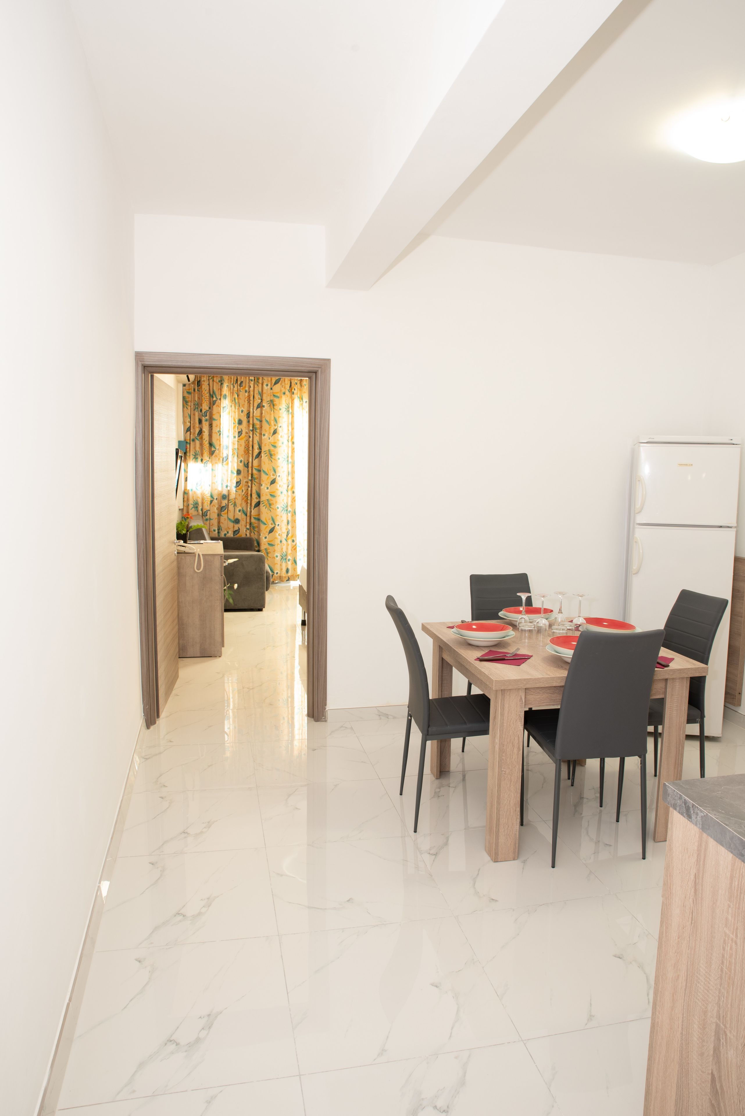 Un coin repas avec une table en bois, des chaises noires et un réfrigérateur blanc.