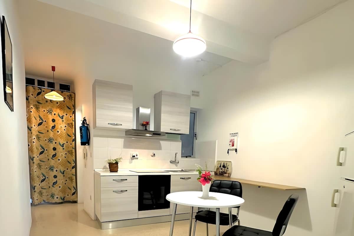 Uma cozinha moderna com armários brancos, um exaustor de aço inoxidável, uma mesa redonda com duas cadeiras pretas e um vaso com flores sobre o balcão.