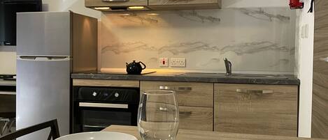 Una cocina moderna con armarios de madera, salpicadero de mármol y zona de comedor dispuesta con platos, vasos y cubiertos.