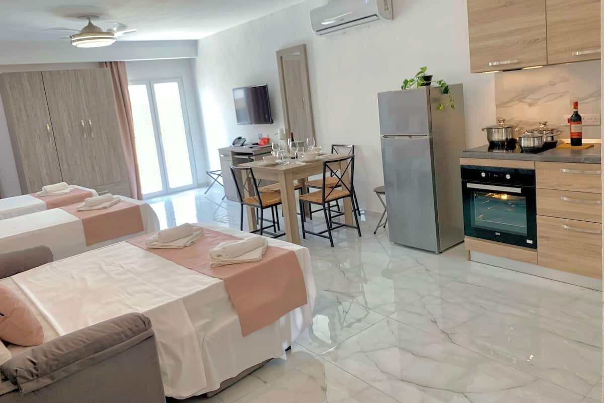 Quarto de hotel moderno com duas camas, área de refeições, cozinha e uma janela grande.