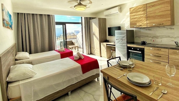 A hotel room with two beds, a dining area, a kitchen, and a large window offering a city view. - For Rest Aparthotel (St. Paul's Bay)