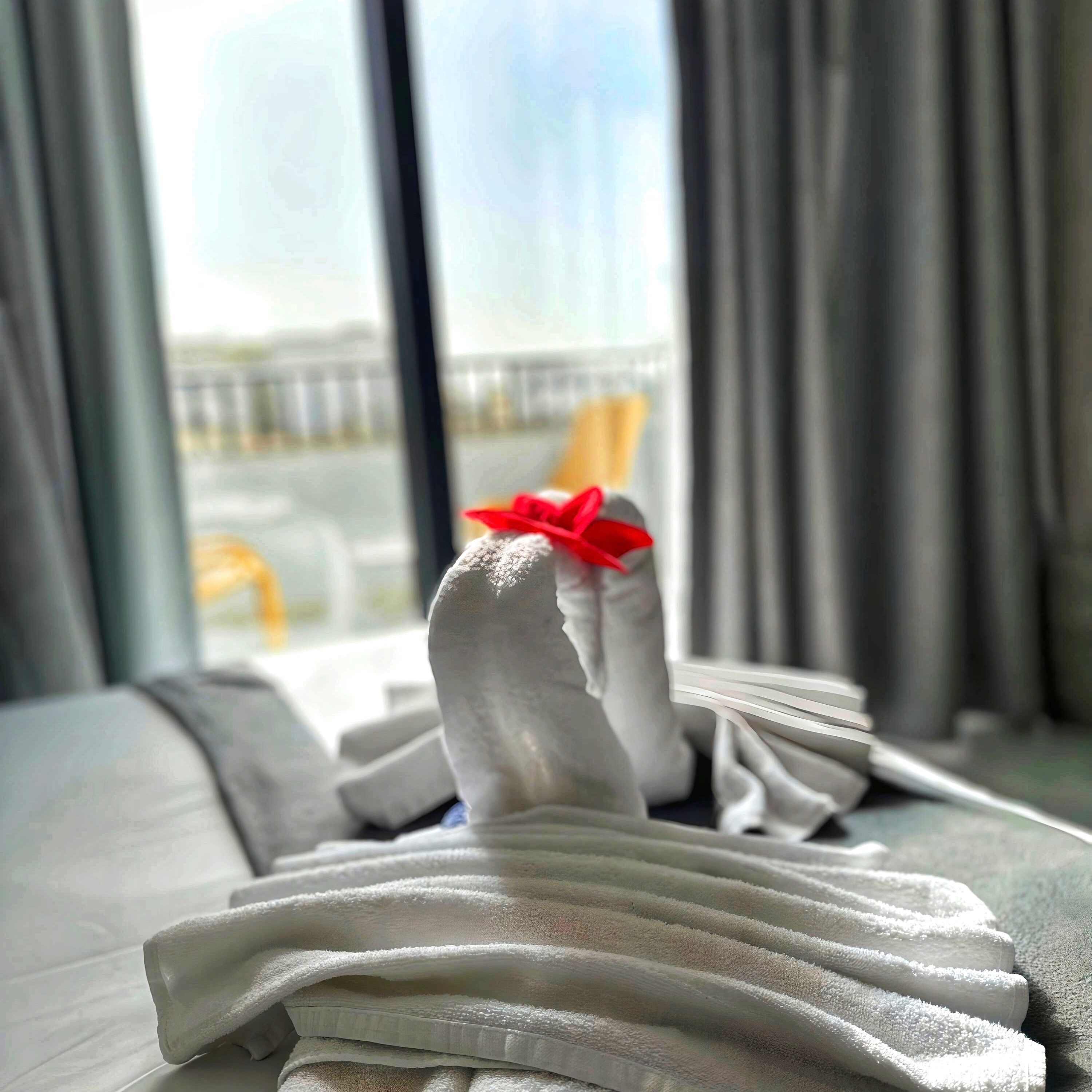 A neatly folded towel with a red bow on a bed in a hotel room.